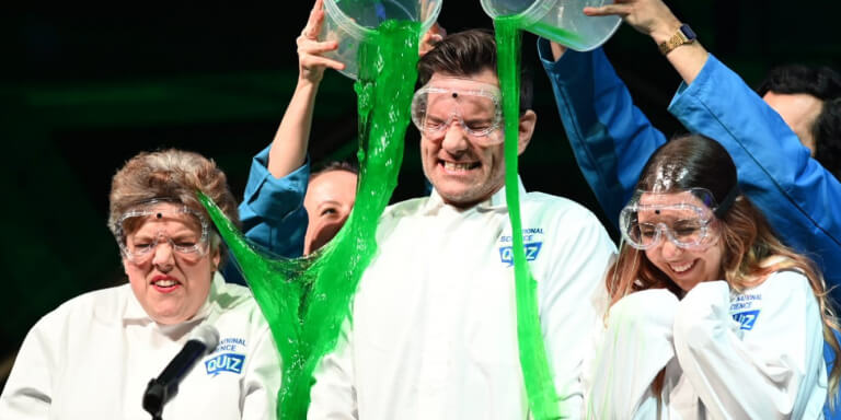 3 adults getting green slime poured on them while wearing National Science Quiz PPE designed by MOO Marketing & Design marketing agency in Melbourne