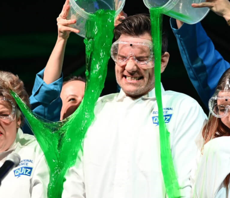 Many getting green slime poured on him while wearing National science Quiz branded PPE designed by MOO Marketing & Design